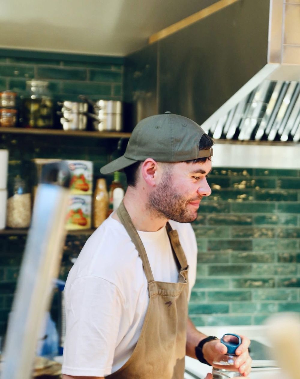 Ryan Bland in a cap and apron, smiling in a tiled kitchen